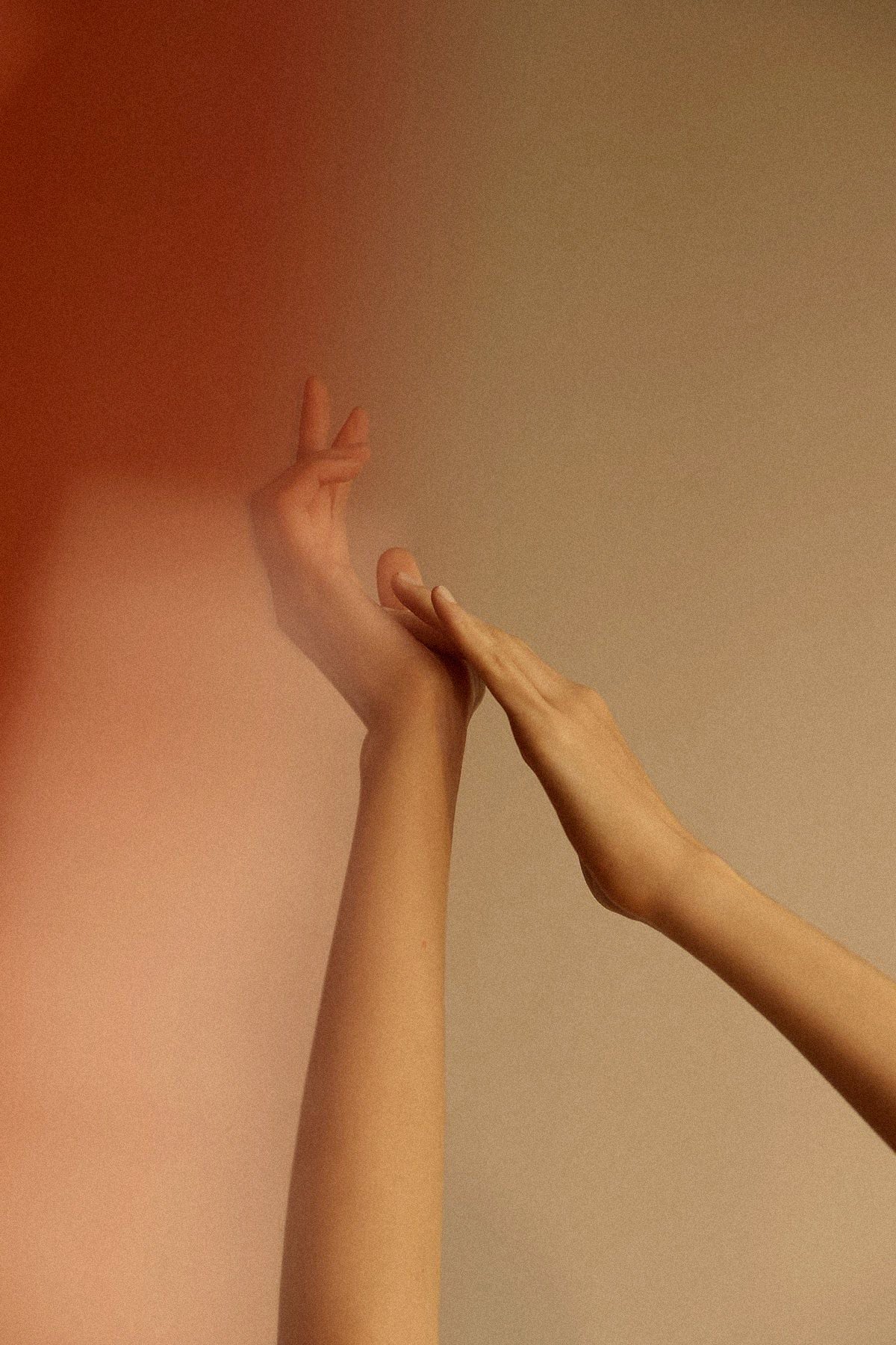 Two arms and hands against a warm beige and terracotta gradient background, with one hand gently touching the other.
