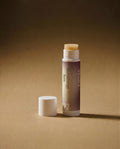 Vesara Calm Aromatherapy Balm tube standing upright with white cap removed and sitting off to the left, both standing on warm beige surface