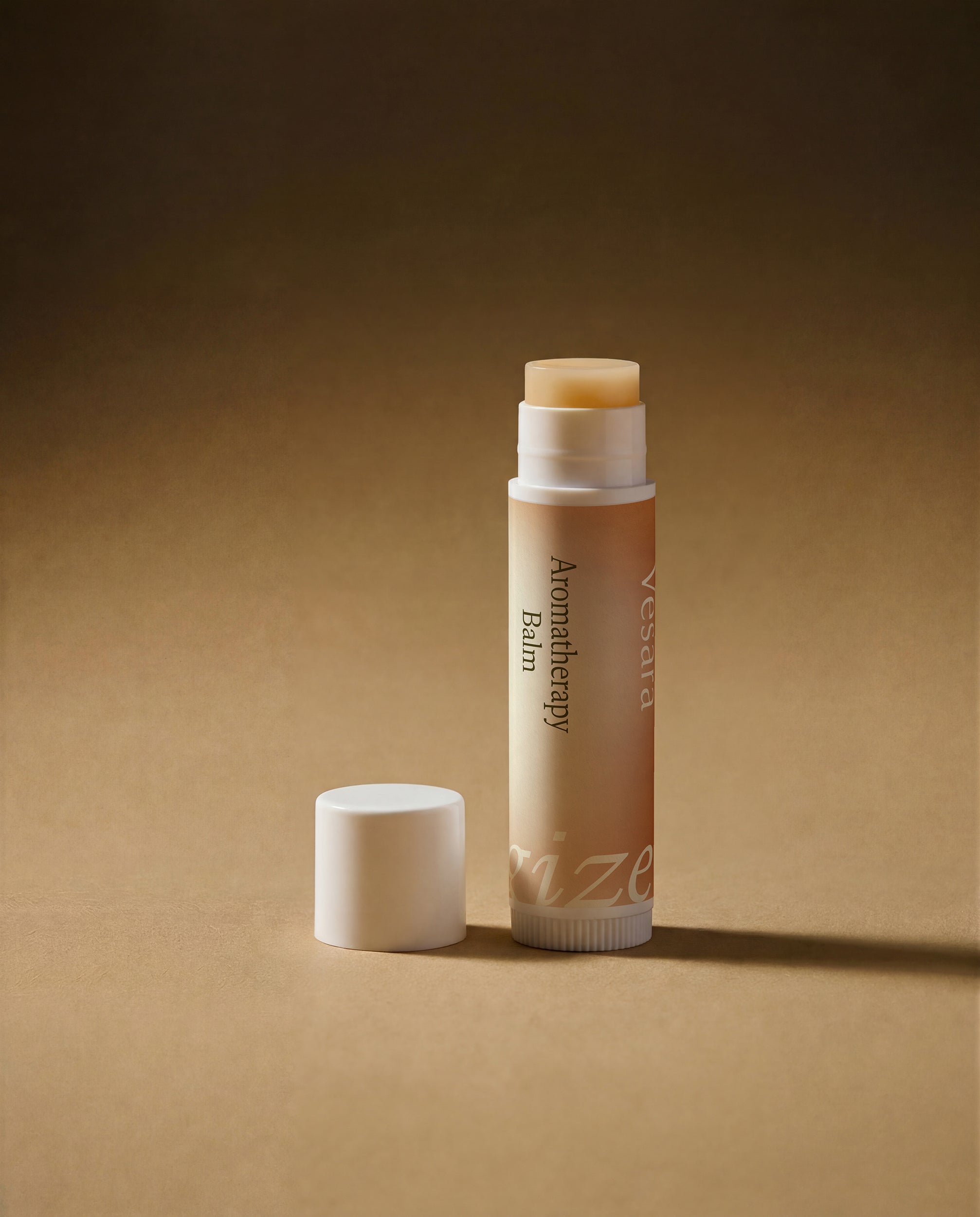 Vesara Energize Aromatherapy Balm tube standing upright with white cap removed and sitting off to the left, both standing on warm beige surface