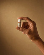 Hand holding Vesara Energize aromatherapy sample size balm tube against a warm beige background