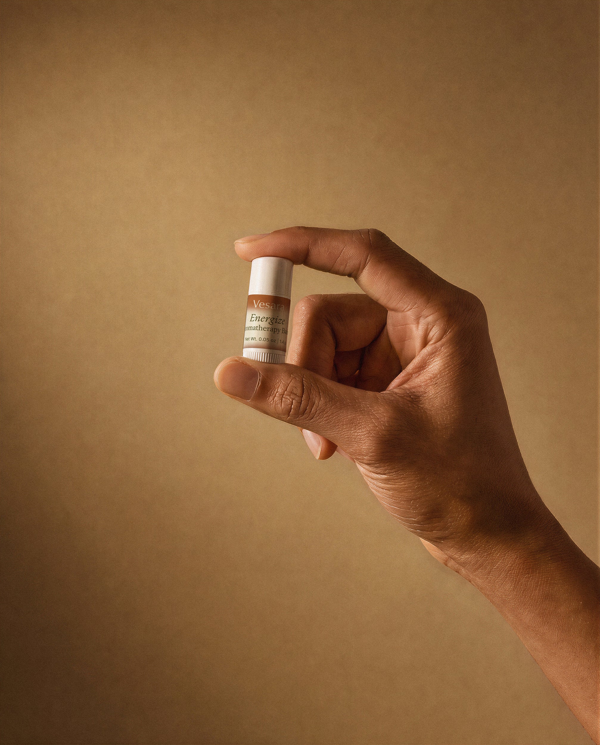 Hand holding Vesara Energize aromatherapy sample size balm tube against a warm beige background
