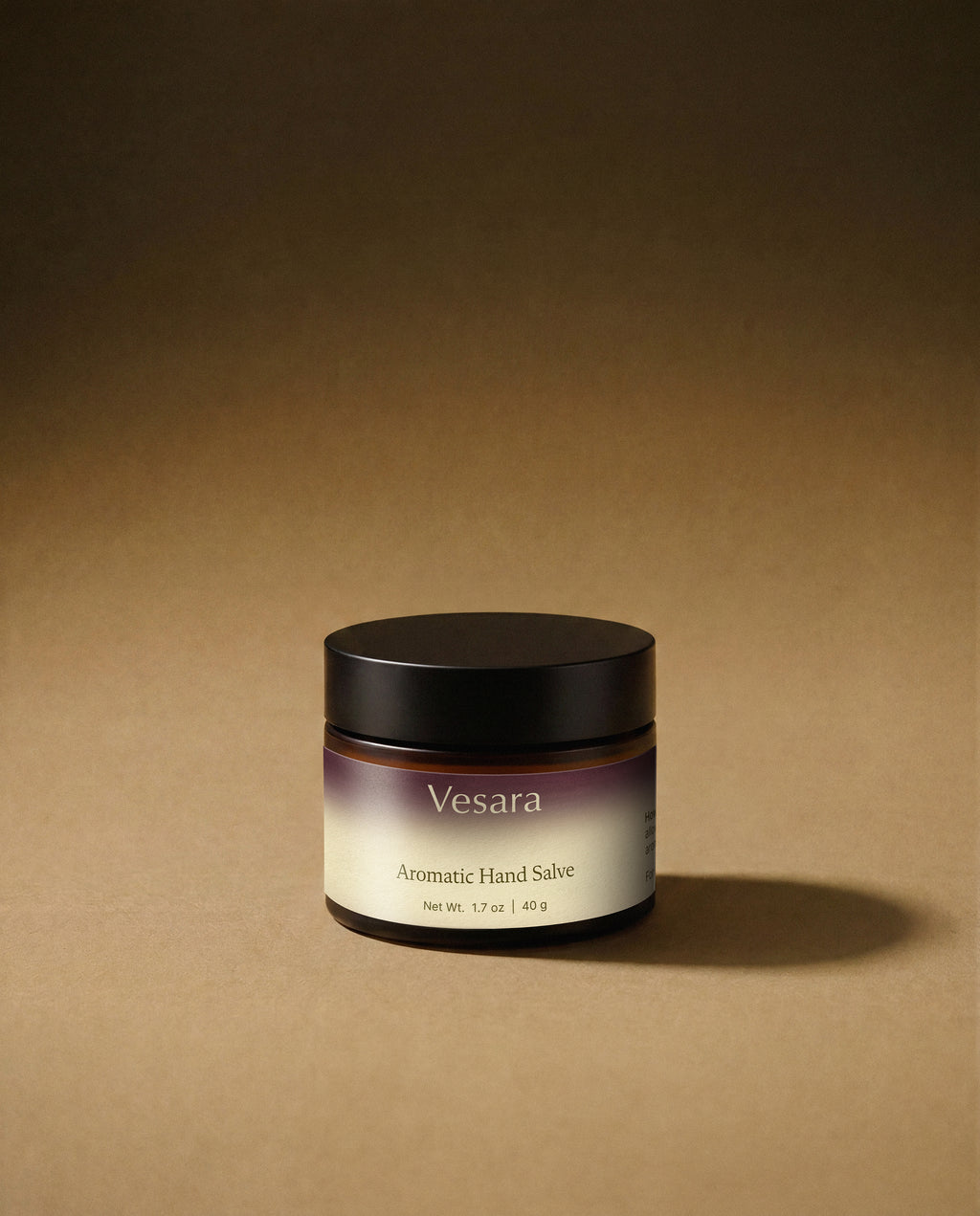 Vesara Calm hand salve round amber glass jar with a black lid against a warm beige background with soft moody studio lighting