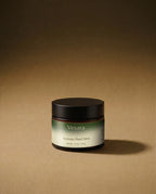 Vesara Clarity hand salve round amber glass jar with a black lid against a warm beige background with soft moody studio lighting