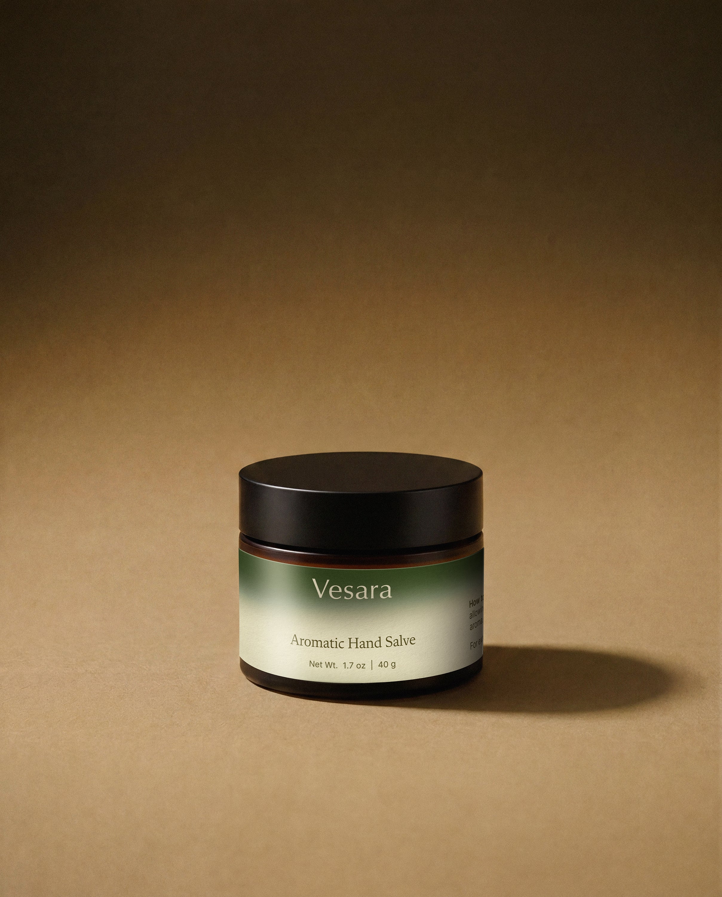 Vesara Clarity hand salve round amber glass jar with a black lid against a warm beige background with soft moody studio lighting