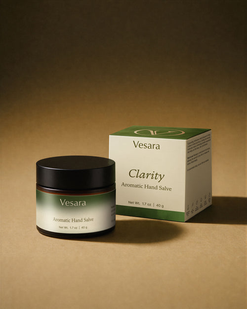 Vesara Clarity hand salve round amber glass jar with a black lid and packaging standing together against a warm beige background with soft moody studio lighting