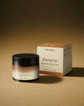 Vesara Energize hand salve round amber glass jar with a black lid and packaging standing together against a warm beige background with soft moody studio lighting