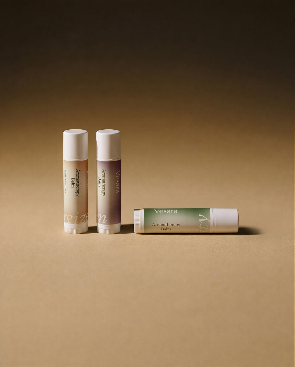 Three Vesara Aromatherapy Balm tubes arranged on warm beige surface two standing upright one lying on its side