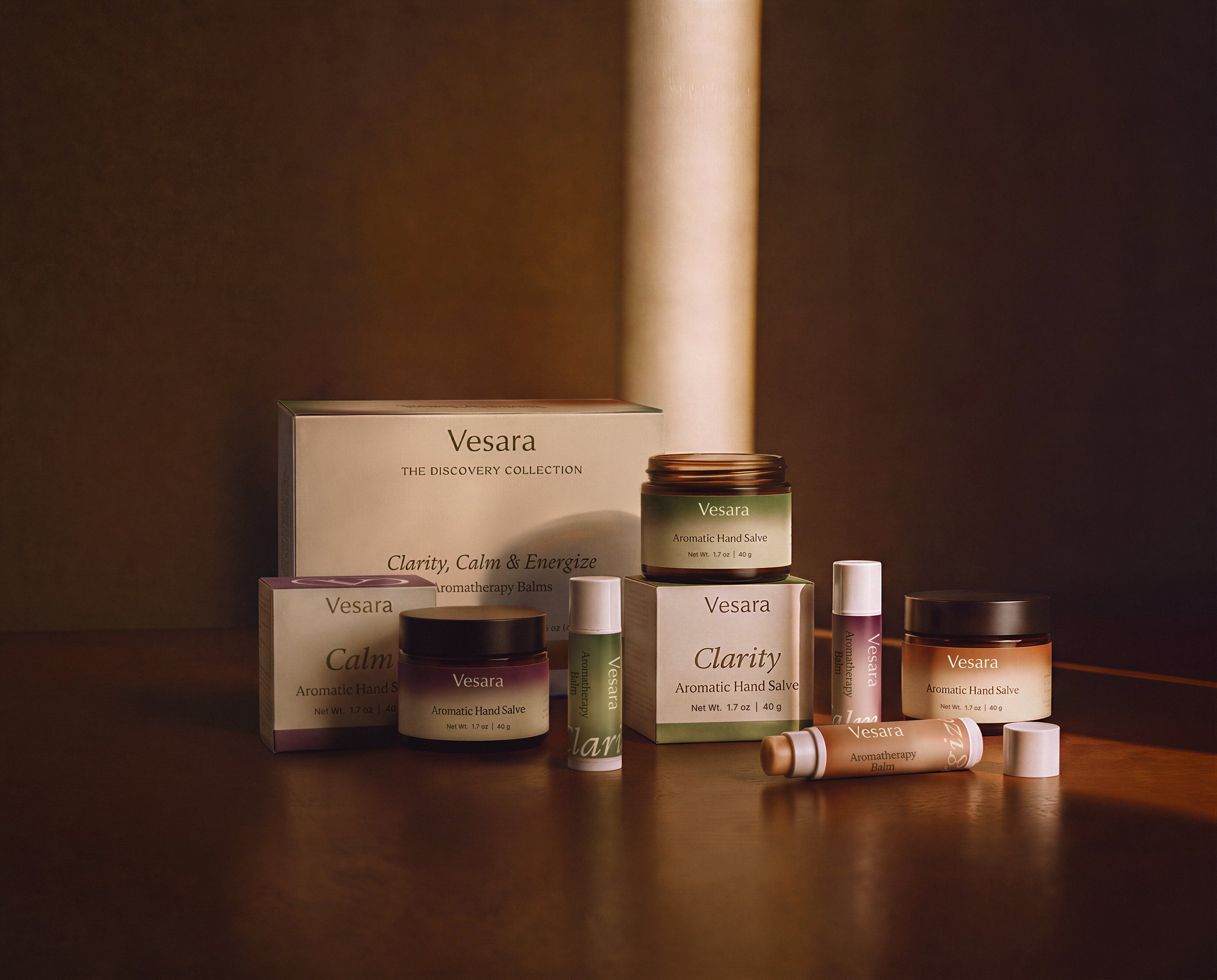 Full Vesara discovery-collection display with aromatic hand salve jars, aromatherapy balm tubes, and product boxes arranged on a dark wood surface