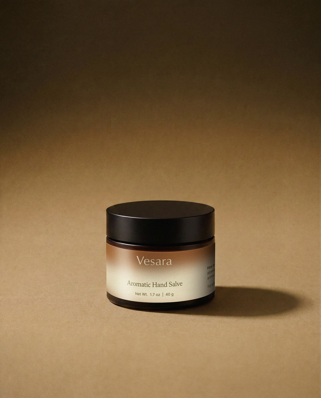 Vesara Energize hand salve round amber glass jar with a black lid against a warm beige background with soft moody studio lighting