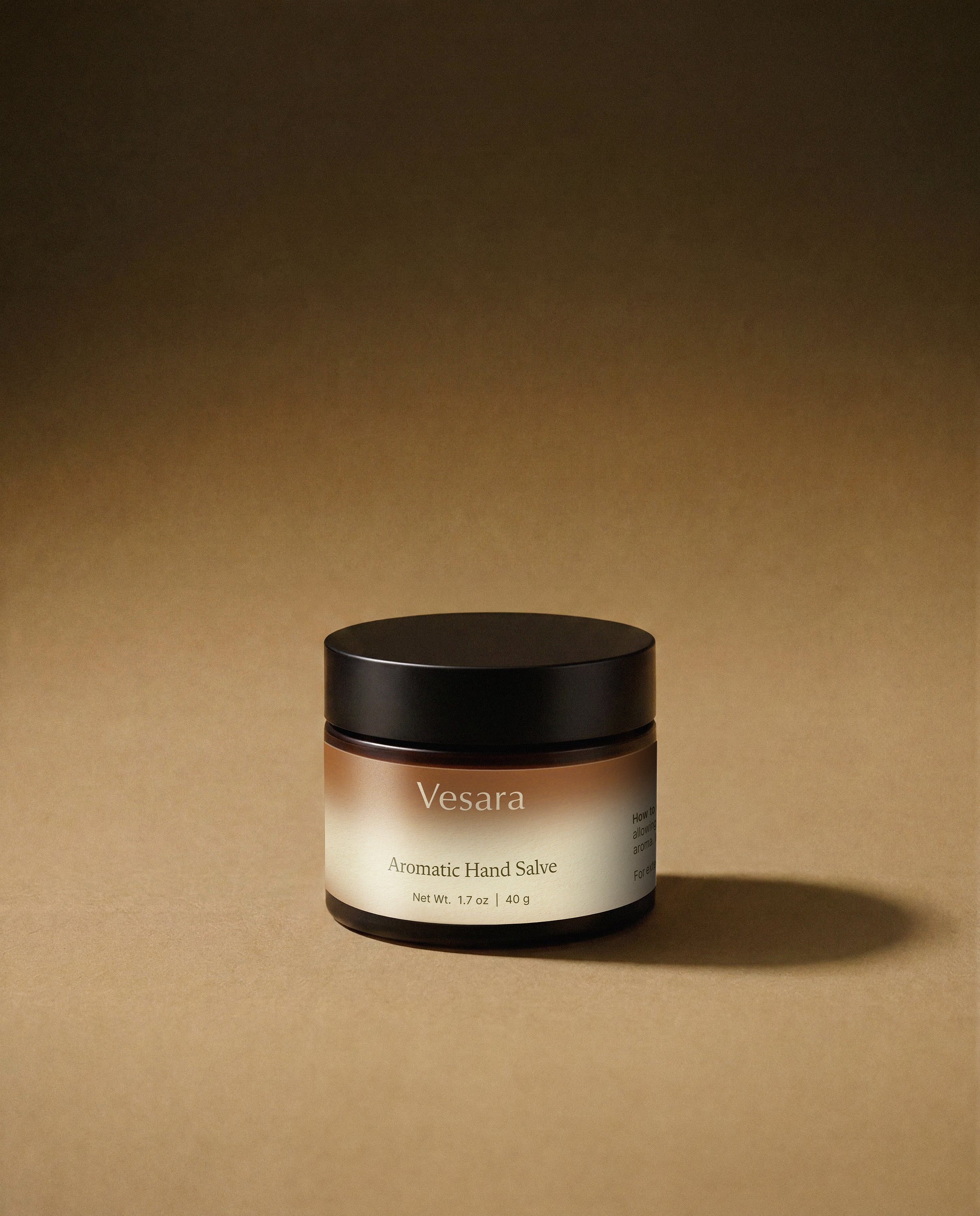 Vesara Energize hand salve round amber glass jar with a black lid against a warm beige background with soft moody studio lighting